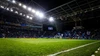 Perspektive vom Spielfeldrand auf den perfekt gepflegten Rasen und die hell erleuchteten Tribünen des Estádio do Dragão bei einem Abendspiel.